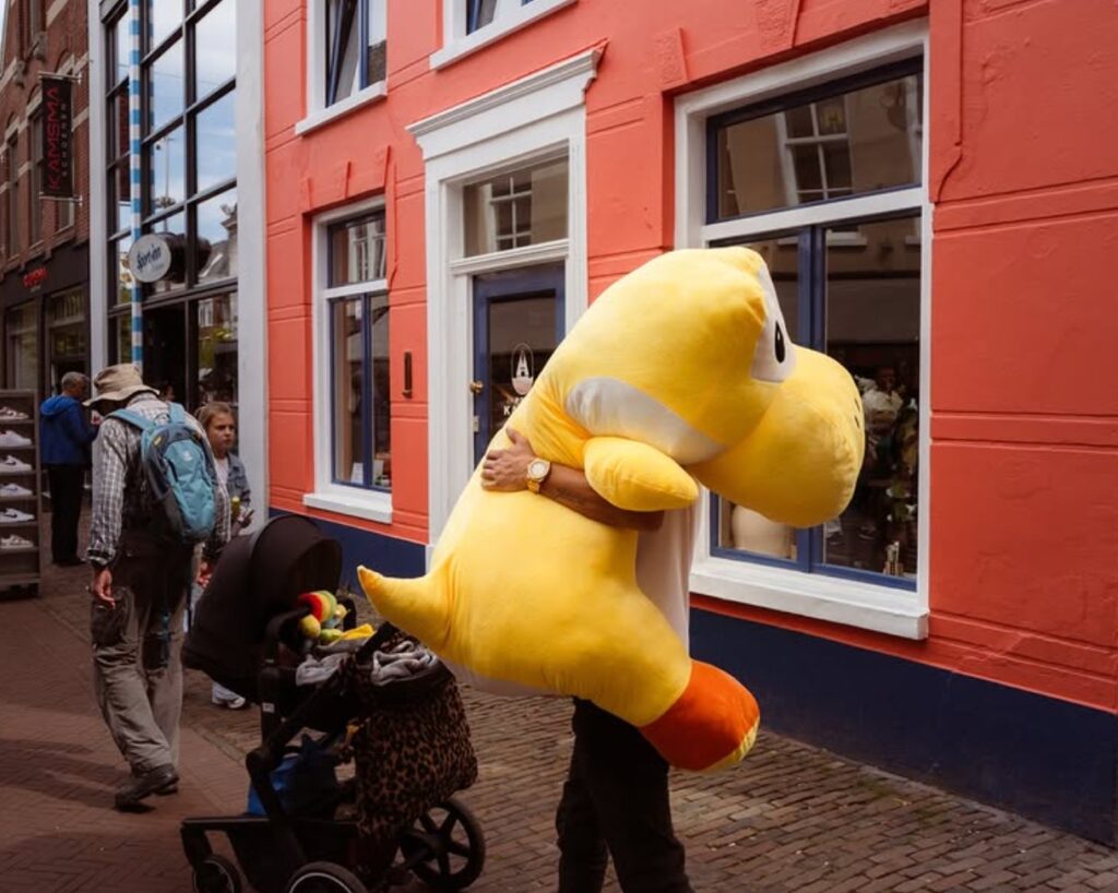 straatfoto van een man idi en grote gele knuffel beet houdt. 